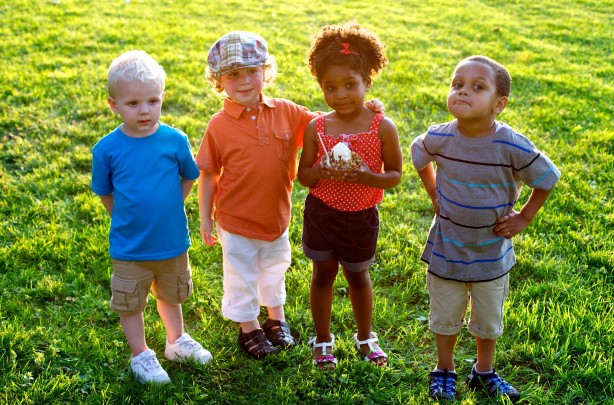 Four children stand on the grass in the sunshine, with the third girl on the left holding a Rita’s branded cup of frozen custard.