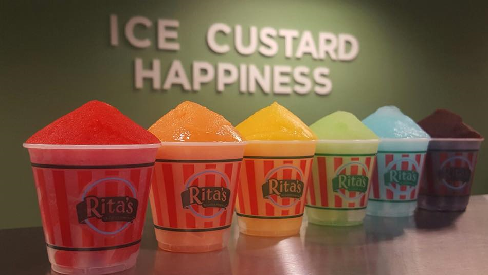 A rainbow of Rita’s ices in branded cups against a green wall that reads, Ice|Custard|Happiness.