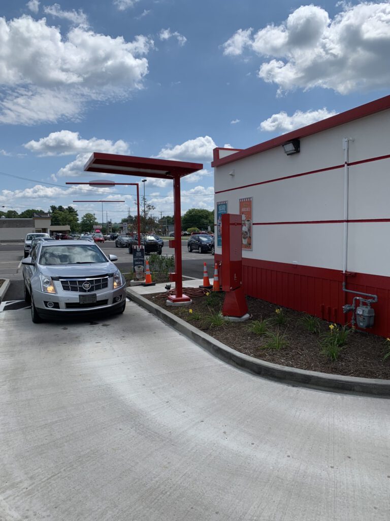 A silver Cadillac sudan waits in line at the drive-thru of a Rita's franchise.