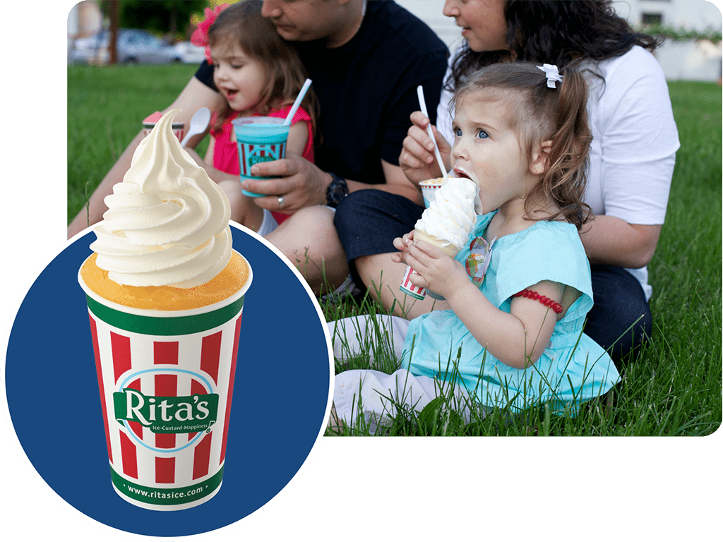 Family sitting on grass eating a Rita's Italian Ice